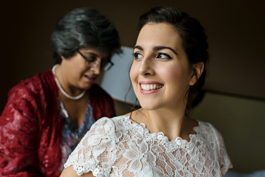 A bride smiles as her mother buttons the back of her wedding dress.